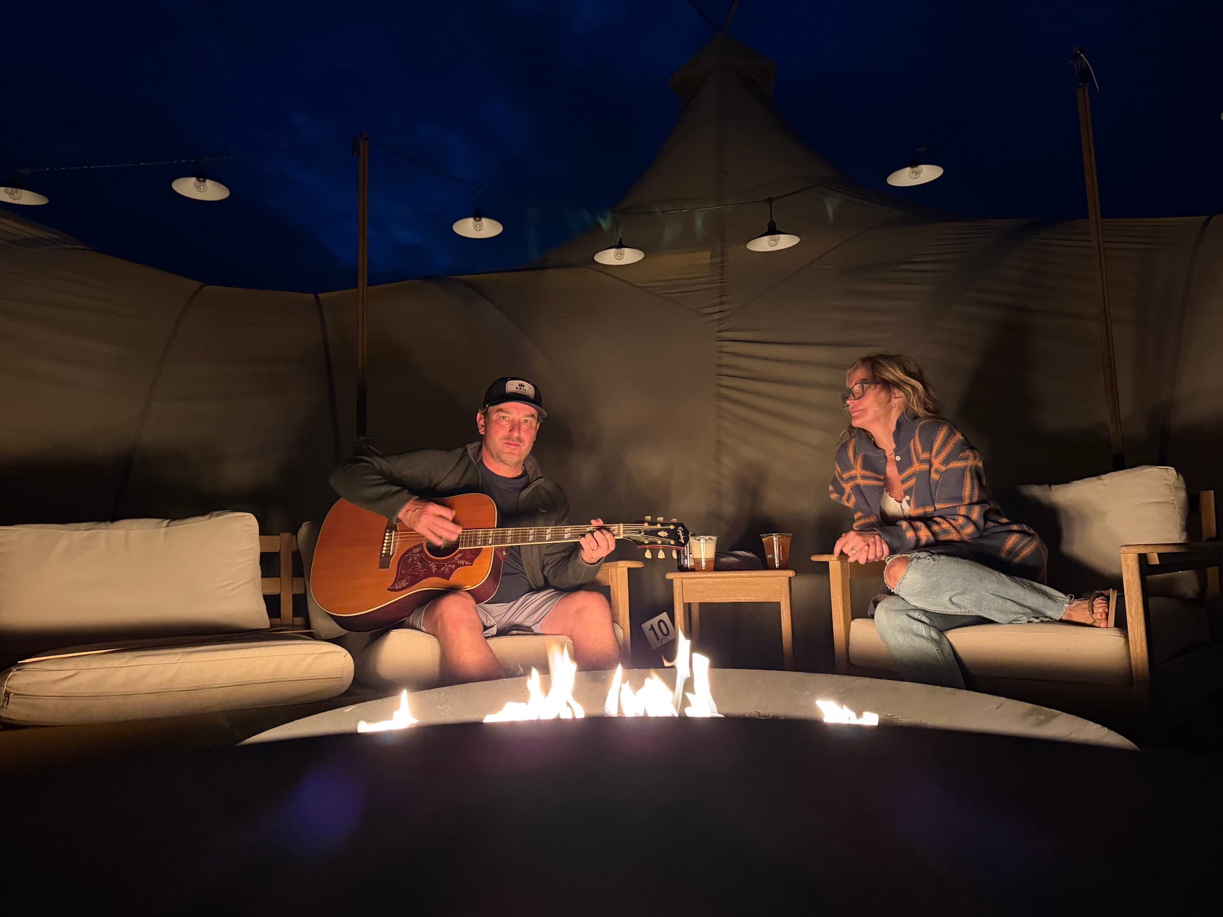 Annie listening as a friend plays guitar by the fire inside a tent
